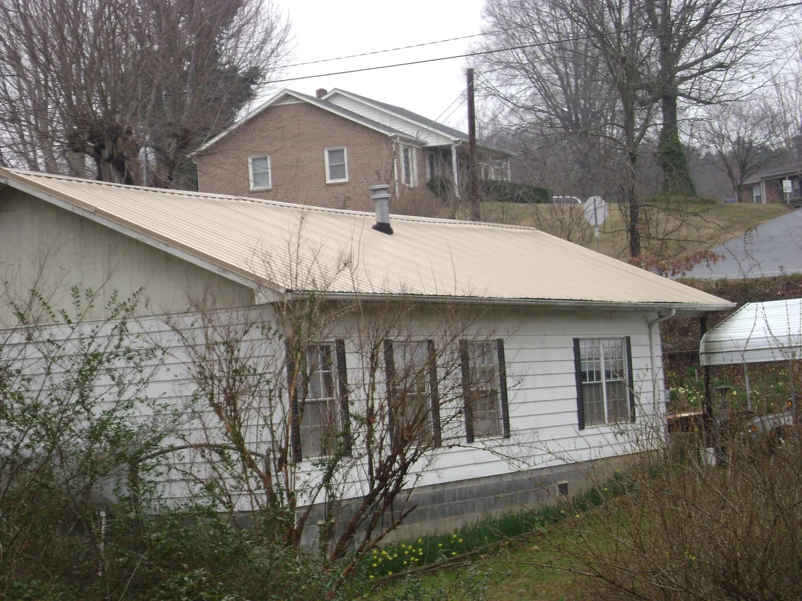 Tan metal roof on a white sided house set into a hillside — Commercial Roofing by Roofing Brothers in Echo